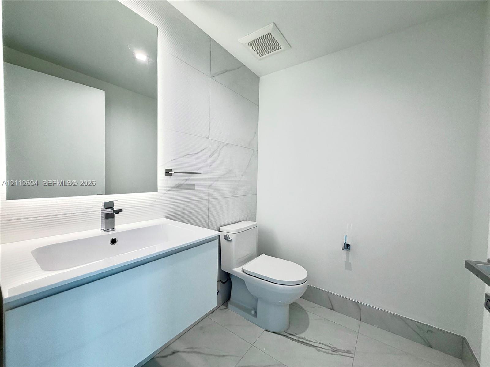 Floating vanity with a rectangular sink, integrated LED mirror, large-format stone-patterned wall tile, and polished metal faucet Floating vanity with a rectangular sink, integrated LED mirror, large-format stone-patterned wall tile, and polished metal faucet