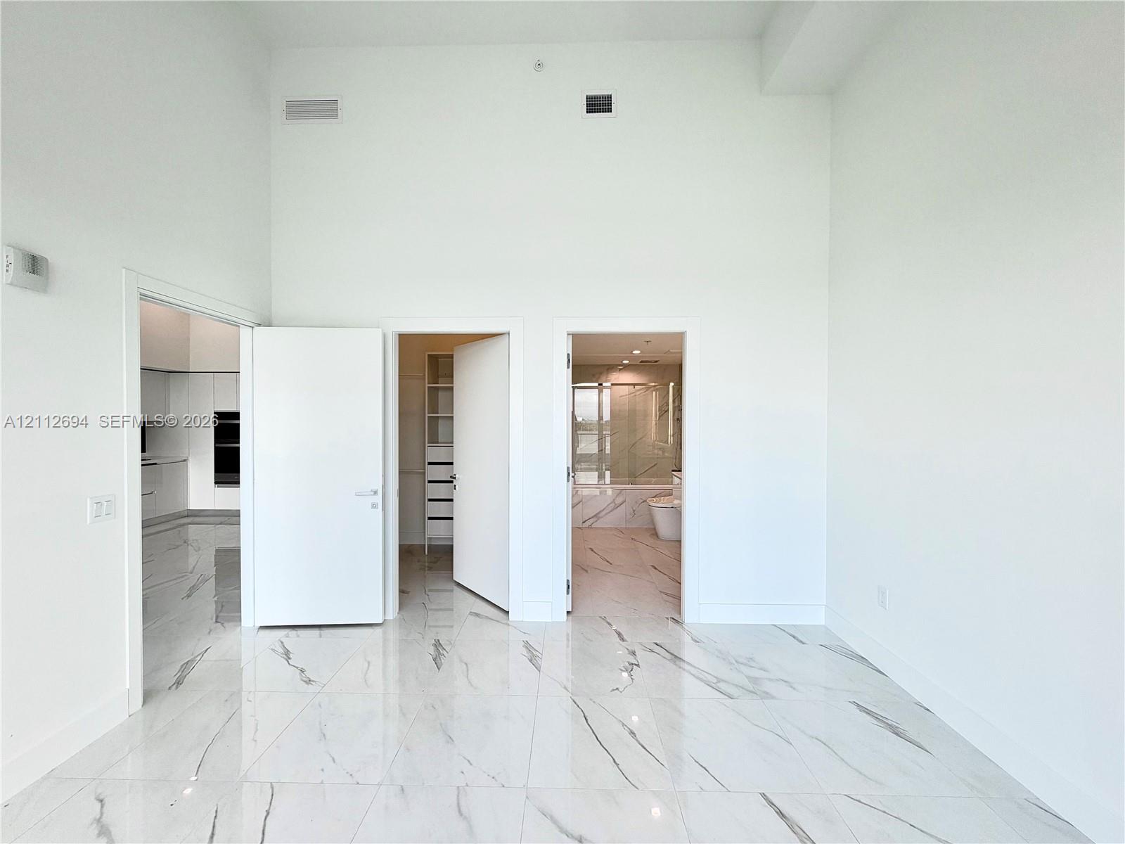 High-ceiling interior featuring polished, large-format stone-patterned tile flooring, minimalist white solid-core doors, and built-in closet shelving High-ceiling interior featuring polished, large-format stone-patterned tile flooring, minimalist white solid-core doors, and built-in closet shelving