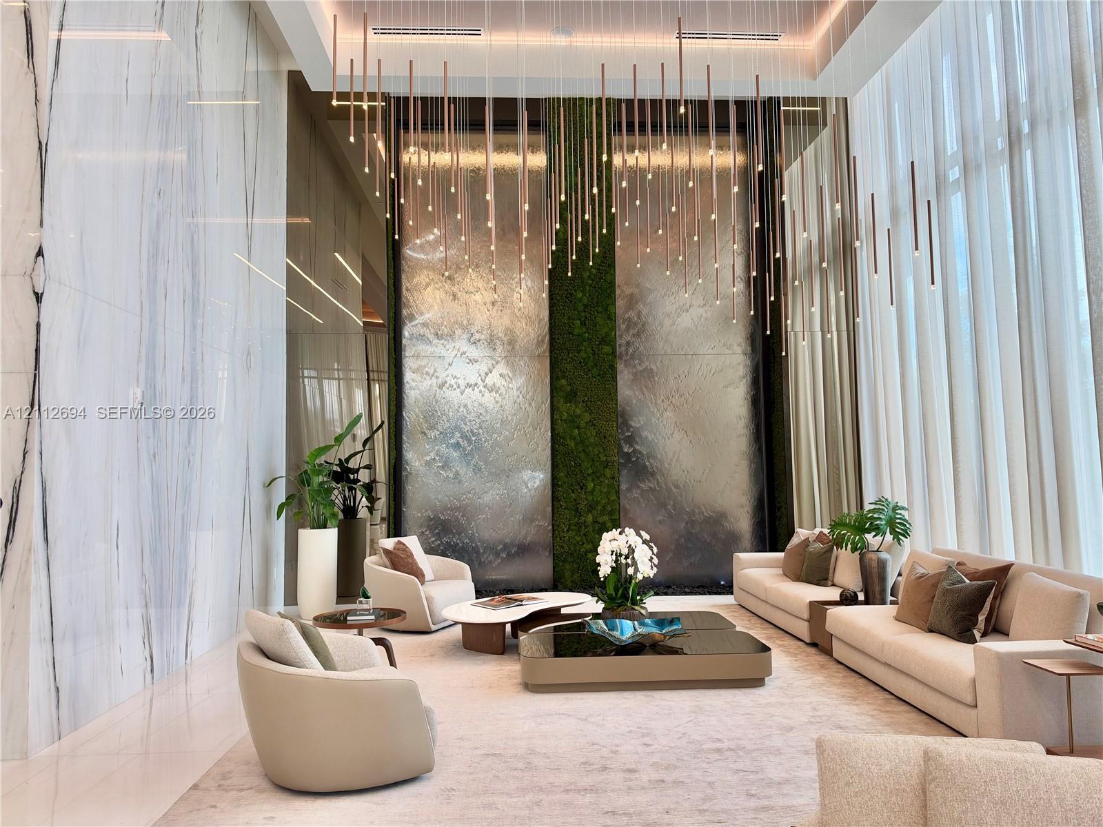 Double-height ceilings featuring large-format stone wall cladding, a floor-to-ceiling interior water feature with moss accents, and a custom multi-pendant light installation