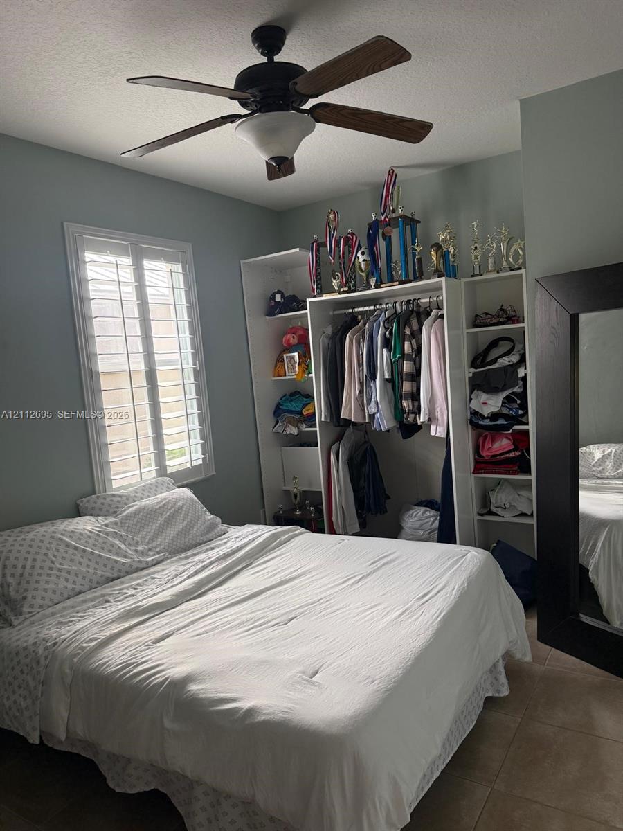 Room featuring white plantation shutters, a multi-blade ceiling fan, and built-in closet cabinetry