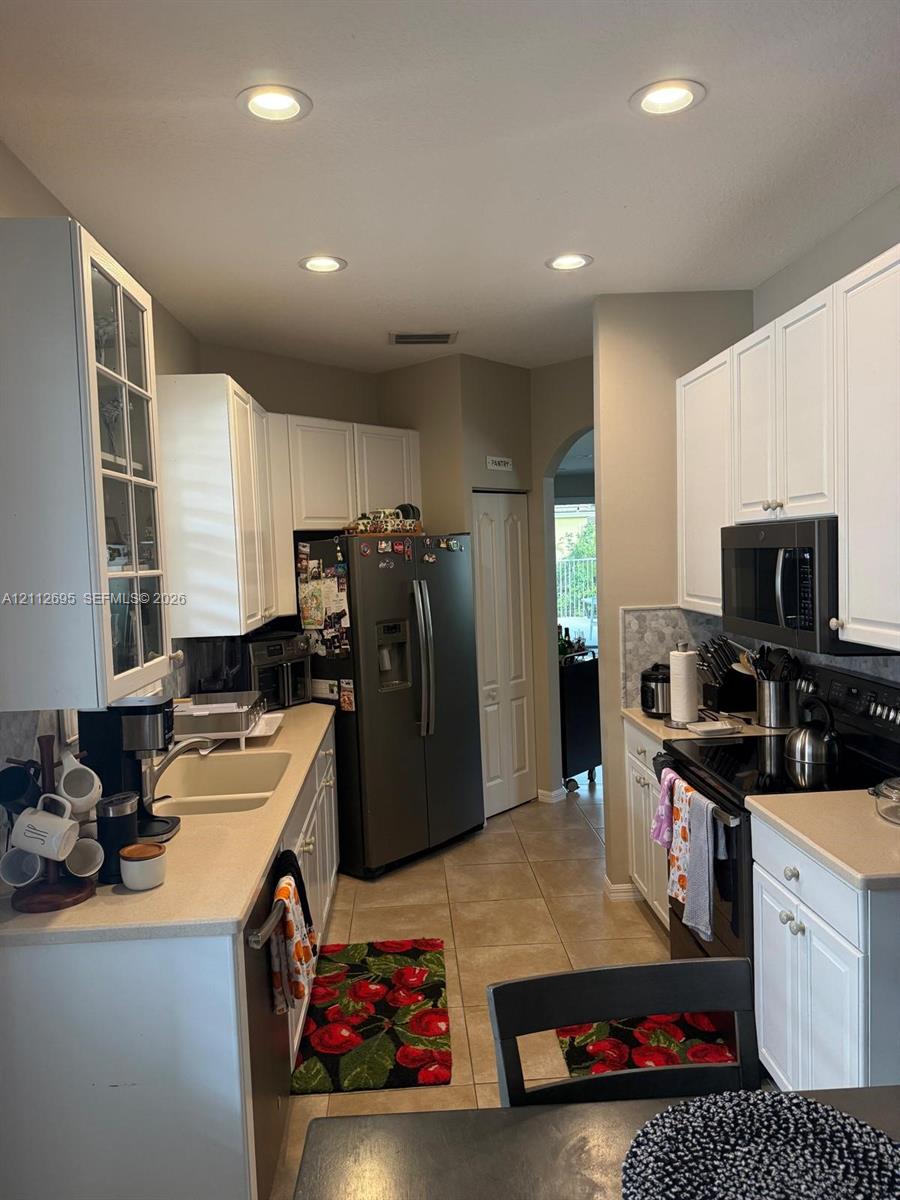 Kitchen featuring white shaker-style cabinetry, solid-surface countertops, recessed lighting, tile flooring, and glass-front upper cabinet doors