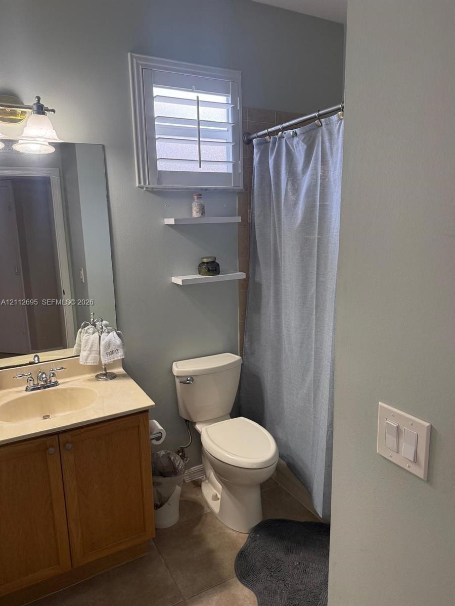 Bathroom featuring a vanity with a neutral-toned integrated sink, wall-mounted white shelving, a window with plantation-style shutters, and a combined tub and shower unit