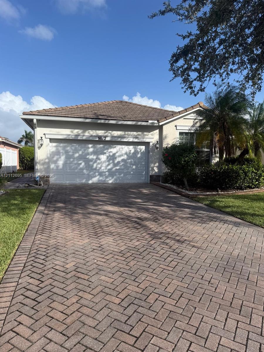 Stucco exterior featuring a tiled roof, herringbone-patterned paver driveway, two-car garage, and wall-mounted coach lighting
