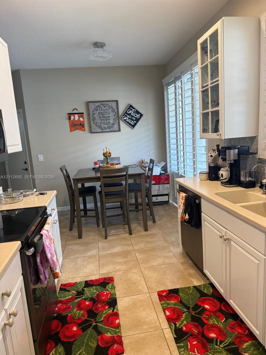 Kitchen featuring white shaker-style cabinetry, a glass-front upper cabinet, solid surface countertops, dual-basin sink, and ceramic tile flooring