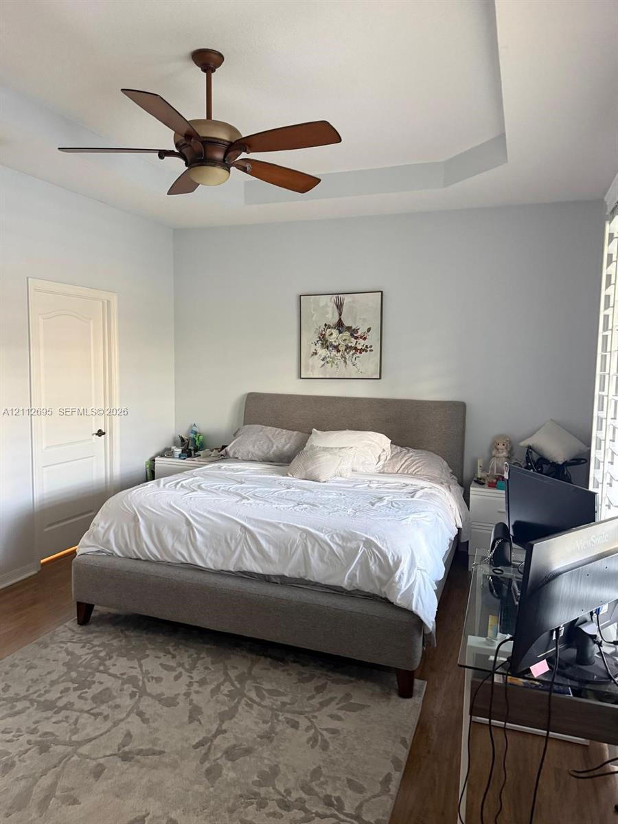 Tray ceiling featuring a central five-blade ceiling fan with integrated lighting and wood-finish flooring
