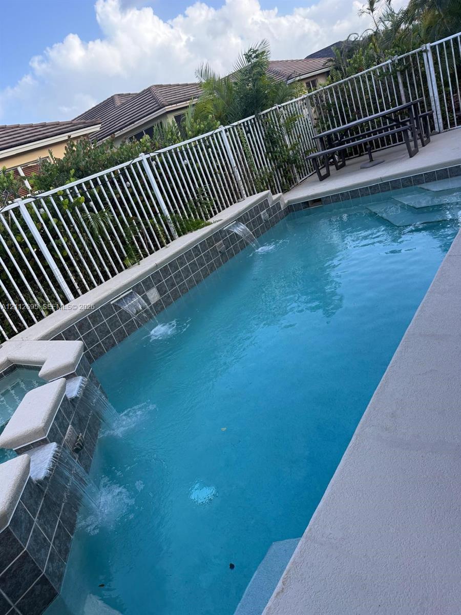 Swimming pool featuring multiple water features, integrated spa, tiled finish, and perimeter metal fencing