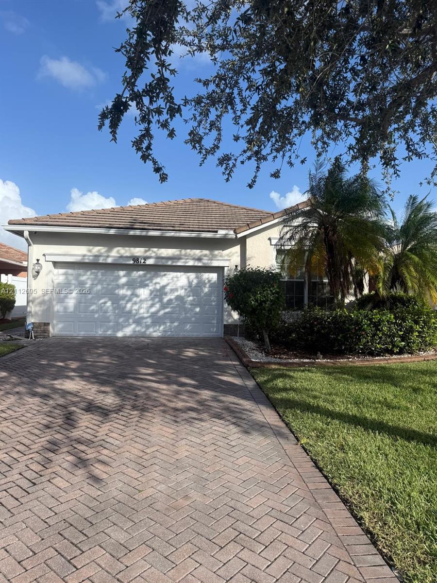 Stucco exterior featuring a tiled hip roof, two-car garage, herringbone-patterned paver driveway, and manicured landscaping Stucco exterior featuring a tiled hip roof, two-car garage, herringbone-patterned paver driveway, and manicured landscaping