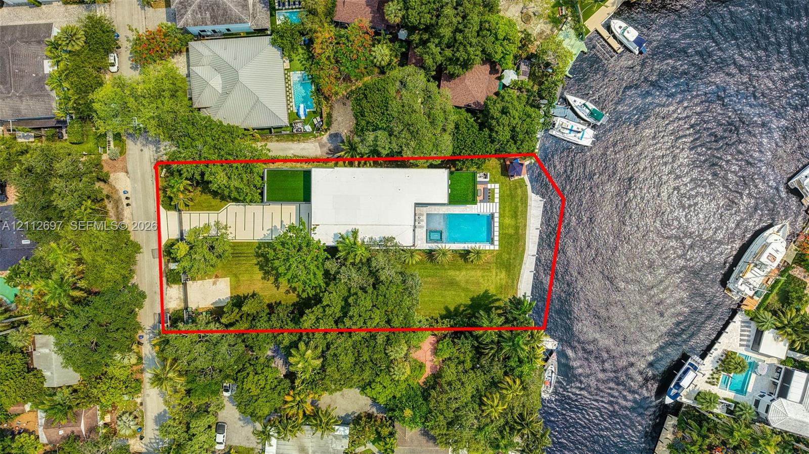 Waterfront property featuring a private dock, rectangular swimming pool, expansive lawn, and paved driveway