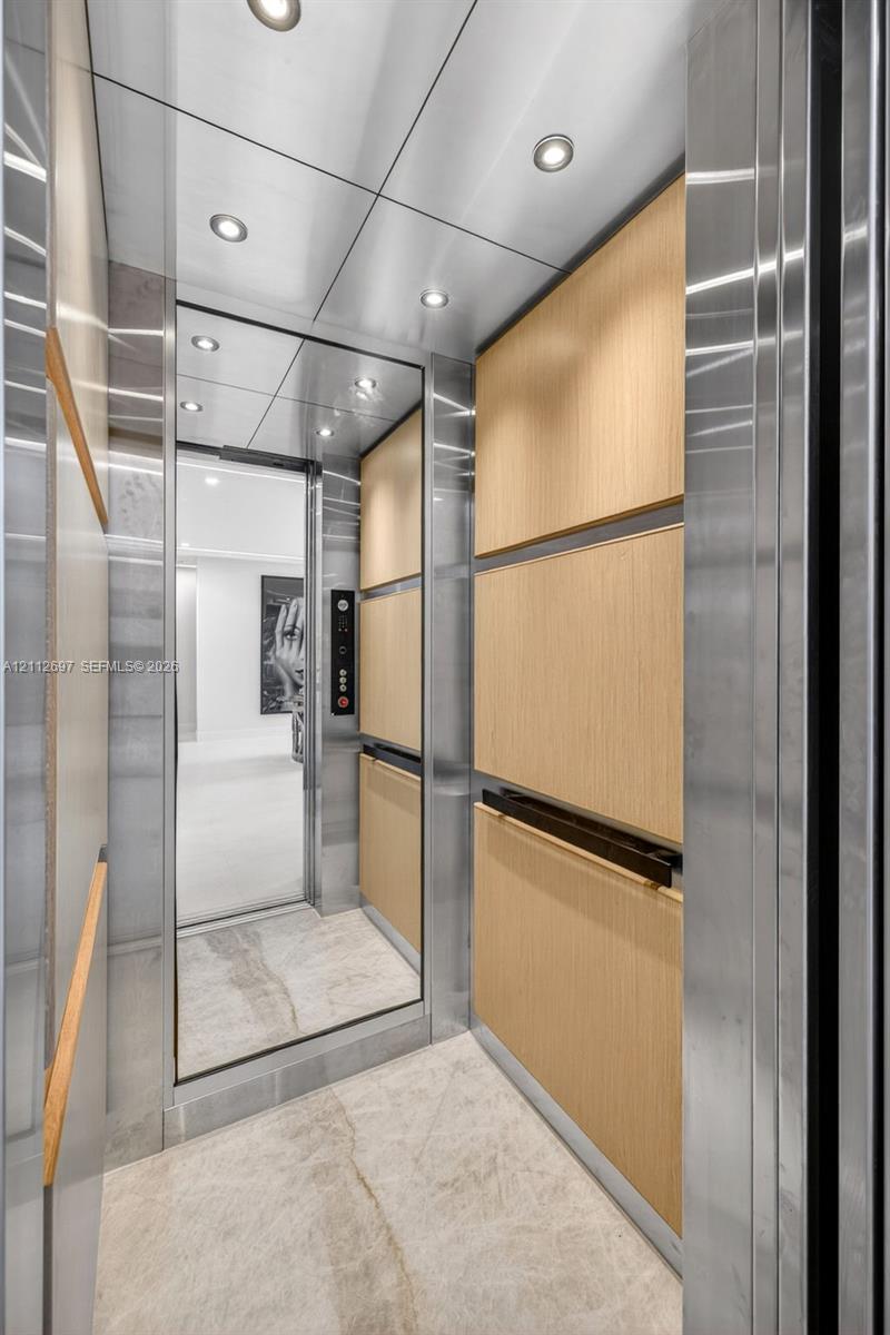 Private elevator cab featuring polished stone flooring, wood-panel wall accents, stainless steel trim, integrated mirror, and recessed ceiling lighting