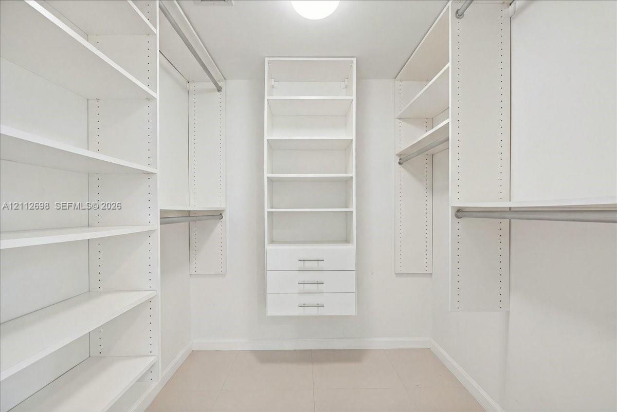 Walk-in closet featuring white built-in shelving, triple-drawer storage unit, metal hanging rods, and tile flooring