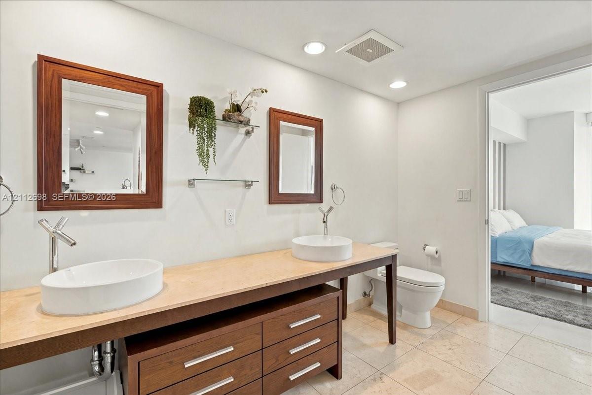 Double vanity featuring a light-toned countertop, two white vessel sinks, wood-finish cabinetry, and wall-mounted faucets