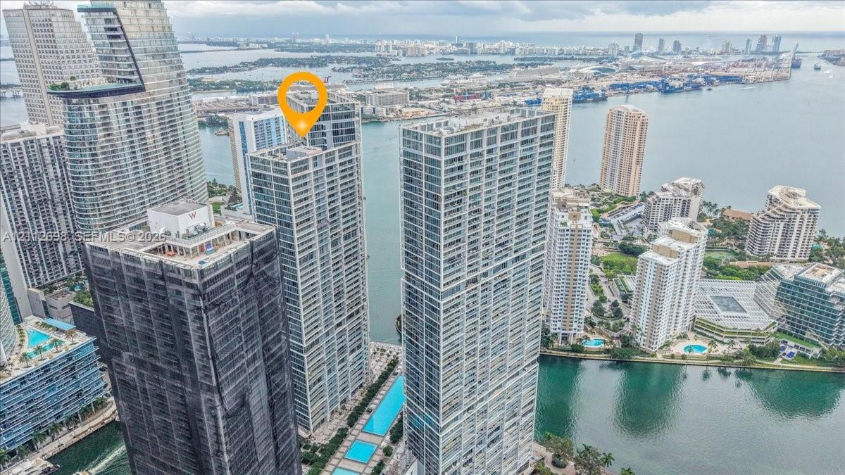 High-rise glass facade residential tower positioned along a coastal waterway, featuring expansive balconies, integrated rooftop pool decks, and floor-to-ceiling glass windows
