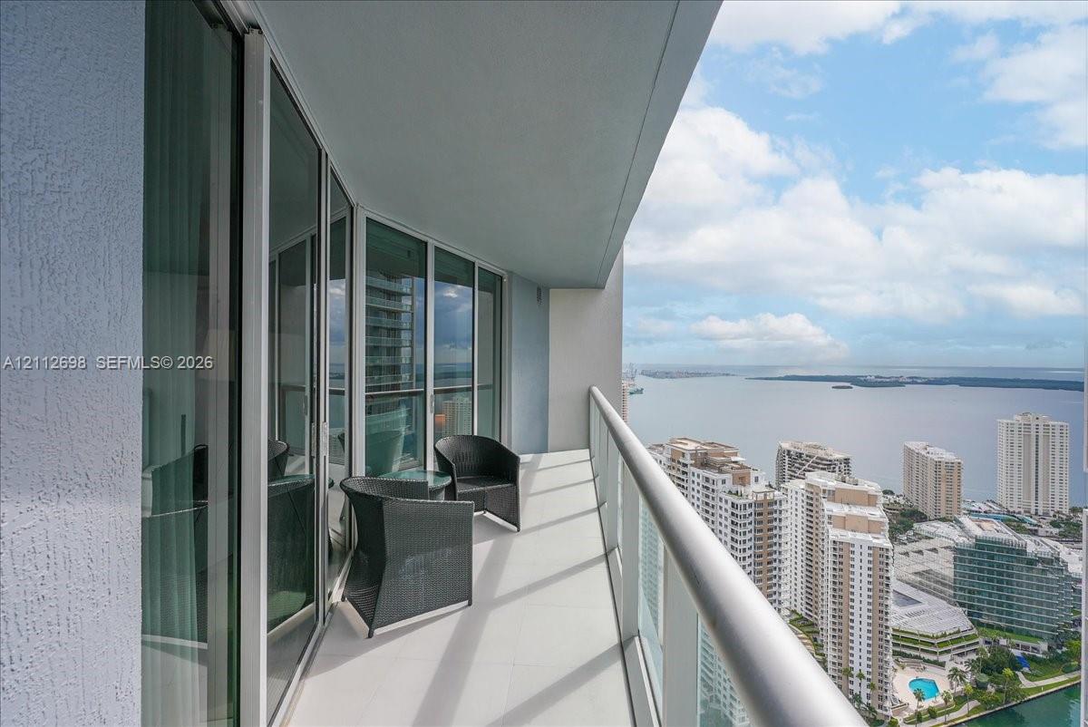 Covered balcony featuring floor-to-ceiling glass doors, a metal railing, and high-rise water and cityscape orientation