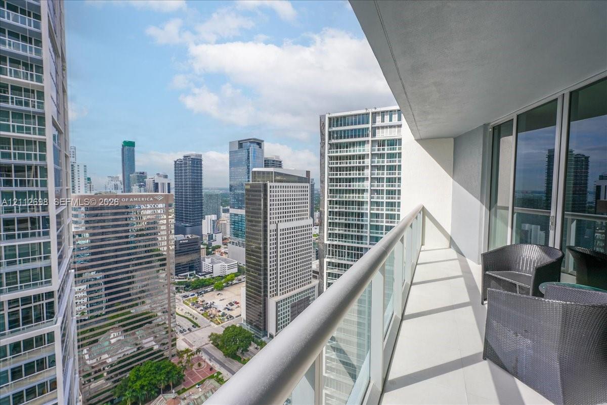 Covered balcony featuring a metal railing with glass panels, concrete flooring, and urban high-rise surroundings