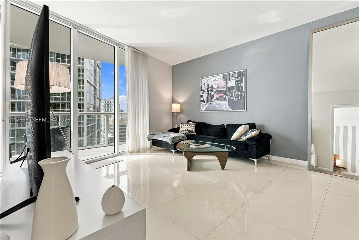 Floor-to-ceiling glass windows, full-height sliding glass balcony door, polished tile flooring, and neutral wall tones