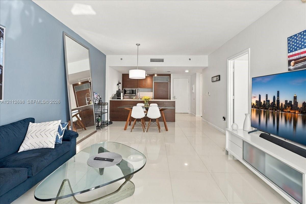 Open-concept interior featuring light-toned tile flooring, recessed lighting, and kitchen cabinetry with a dark wood-finish