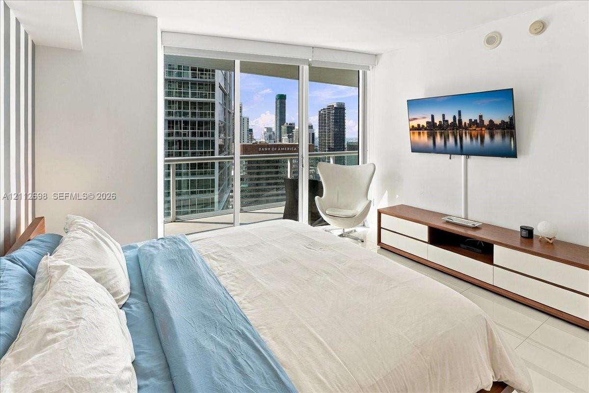 Floor-to-ceiling sliding glass doors, white tile flooring, and a private balcony featuring a metal railing