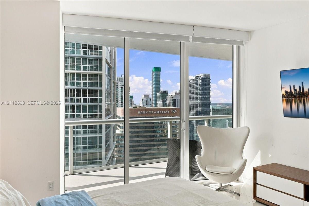 Floor-to-ceiling glass sliding doors opening to a private balcony with metal railings, offering an urban skyline panorama