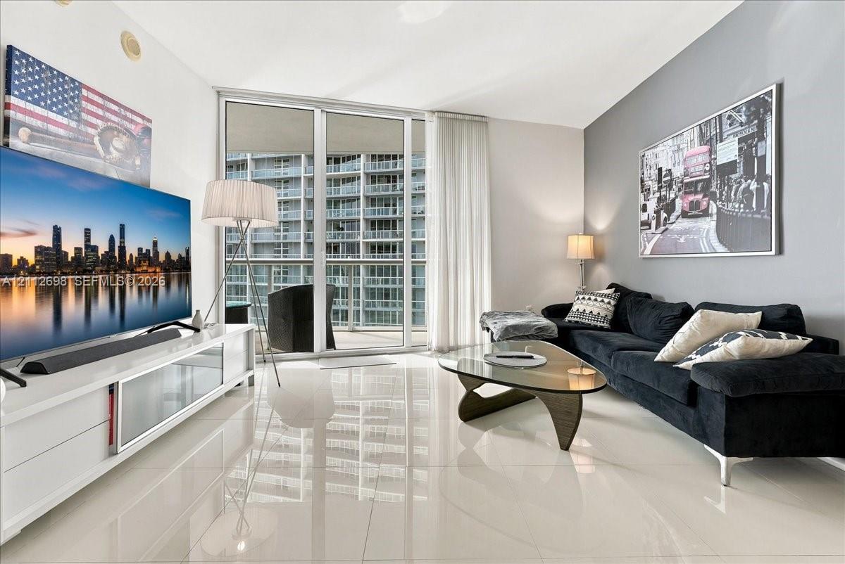 Living space featuring large-format tile flooring, floor-to-ceiling glass sliding doors, and a decorative accent wall