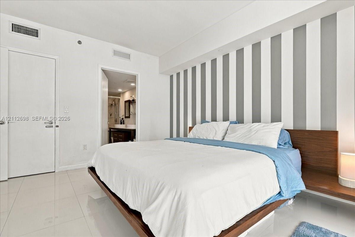 Polished tile flooring, vertical wall accent detailing, and built-in wood-finish headboard with integrated side tables