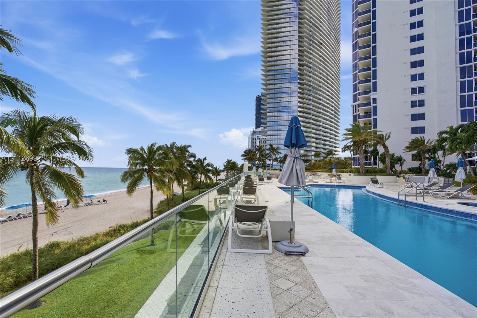 Oceanfront swimming pool with tiled surround, glass panel railing, and direct sandy beach access