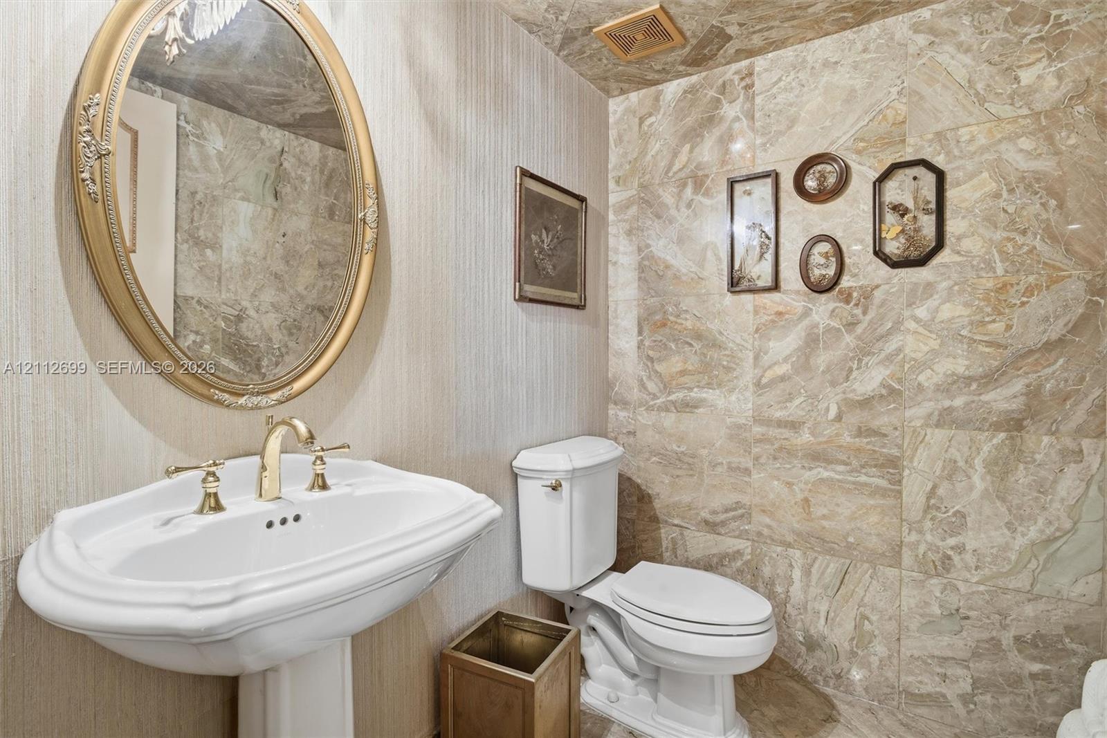 Guest half a bathroom features, beautiful marble walls and ceiling, pedestal sink with brass-finish faucet, and a beautiful wall-mounted mirror