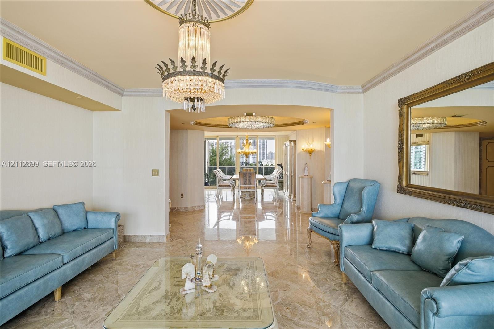 Polished stone flooring, ornate crystal chandelier, recessed ceiling medallion, decorative crown molding, and expansive floor-to-ceiling windows