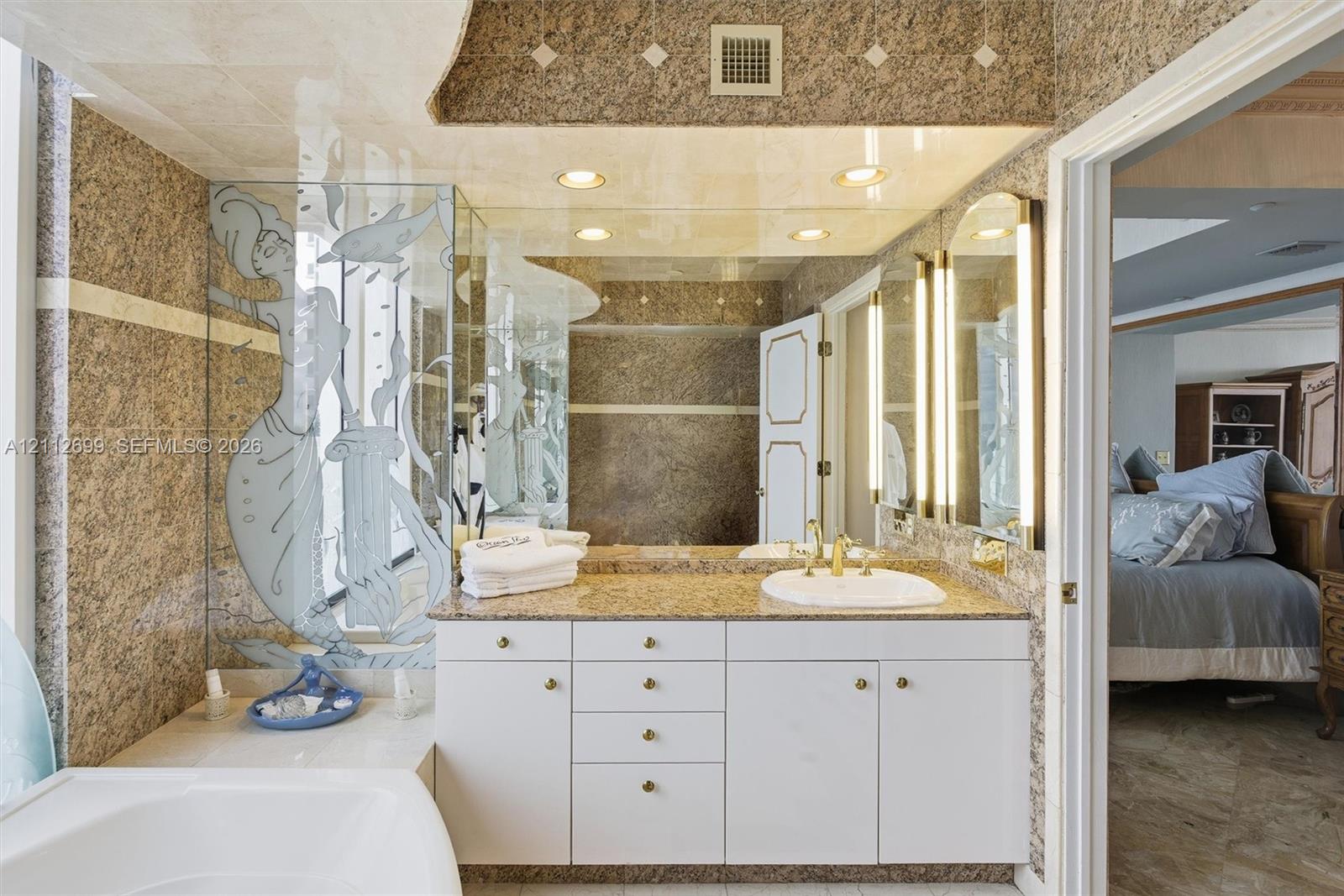 Full-wall marble tilling, white vanity cabinetry with stone countertop, and integrated vertical lighting