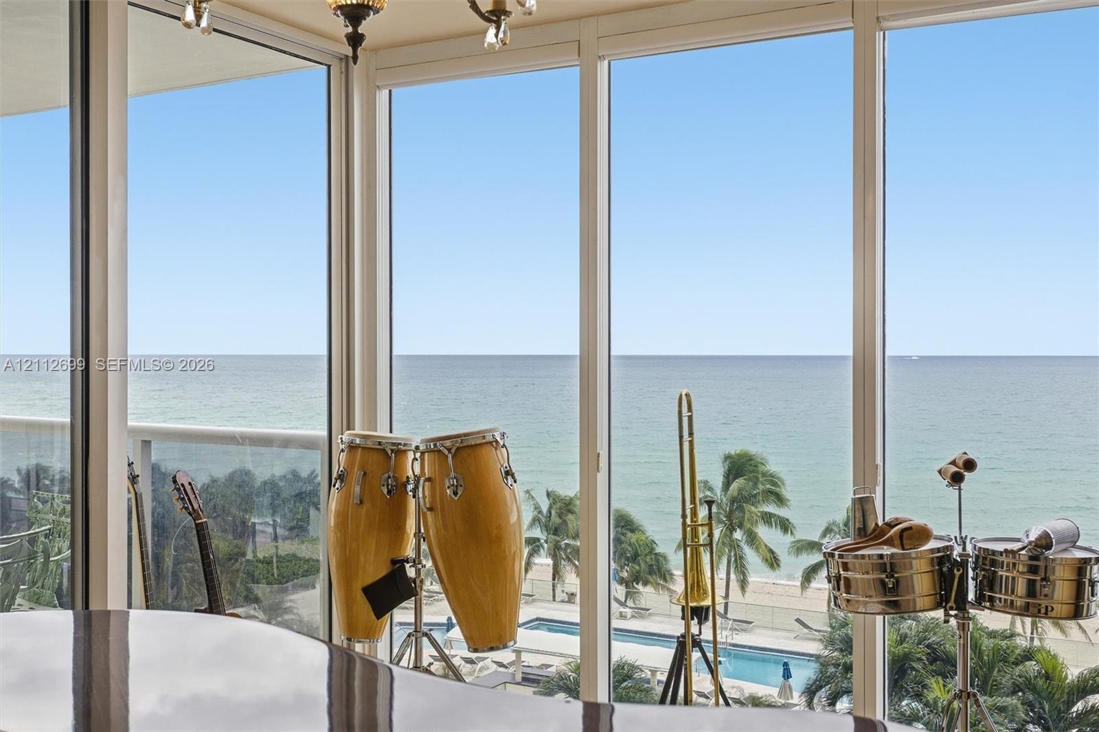 Floor-to-ceiling windows featuring panoramic oceanfront exposure, exterior balcony with railing, and integrated overhead lighting fixture
