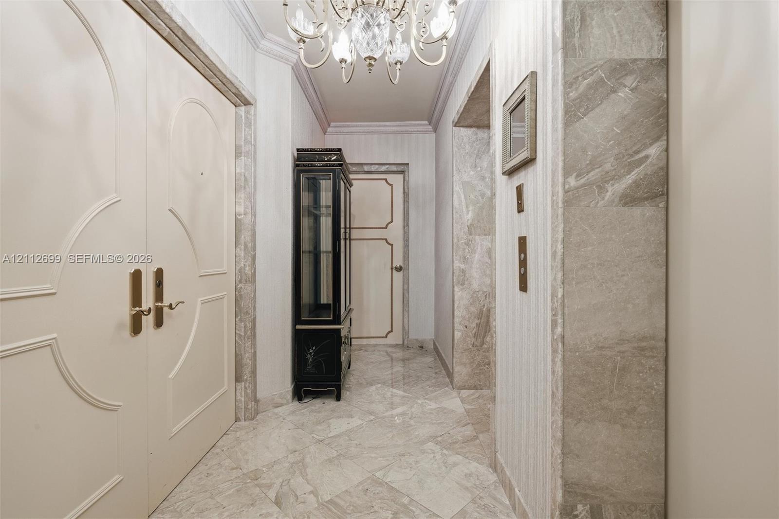 Entryway from a private elevator lobby. Featuring double doors with decorative millwork, stone tile flooring, crown molding, and stone wall accents