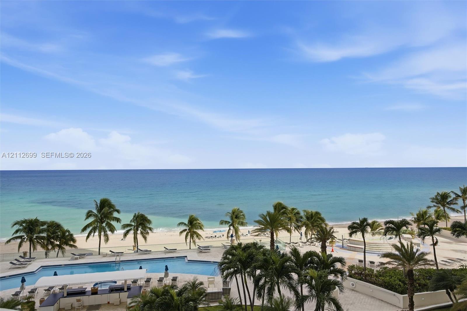Oceanfront property featuring a swimming pool, paved pool deck, and landscaped palm trees
