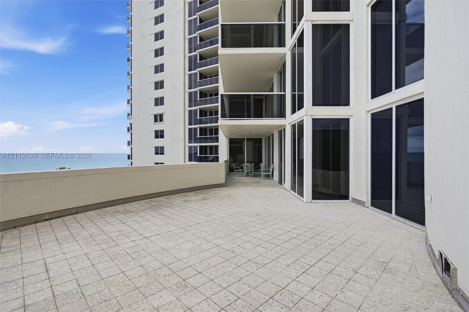 Expansive tiled terrace featuring a solid-surface perimeter wall, floor-to-ceiling glass windows, and sliding glass doors