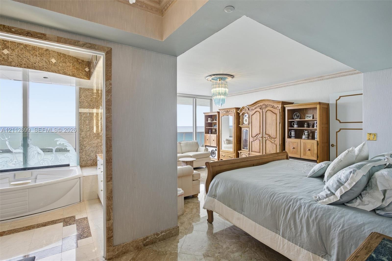 Polished stone flooring, crown molding, built-in recessed lighting, decorative crystal-style chandelier, and jetted corner soaking tub featuring stone tile surround