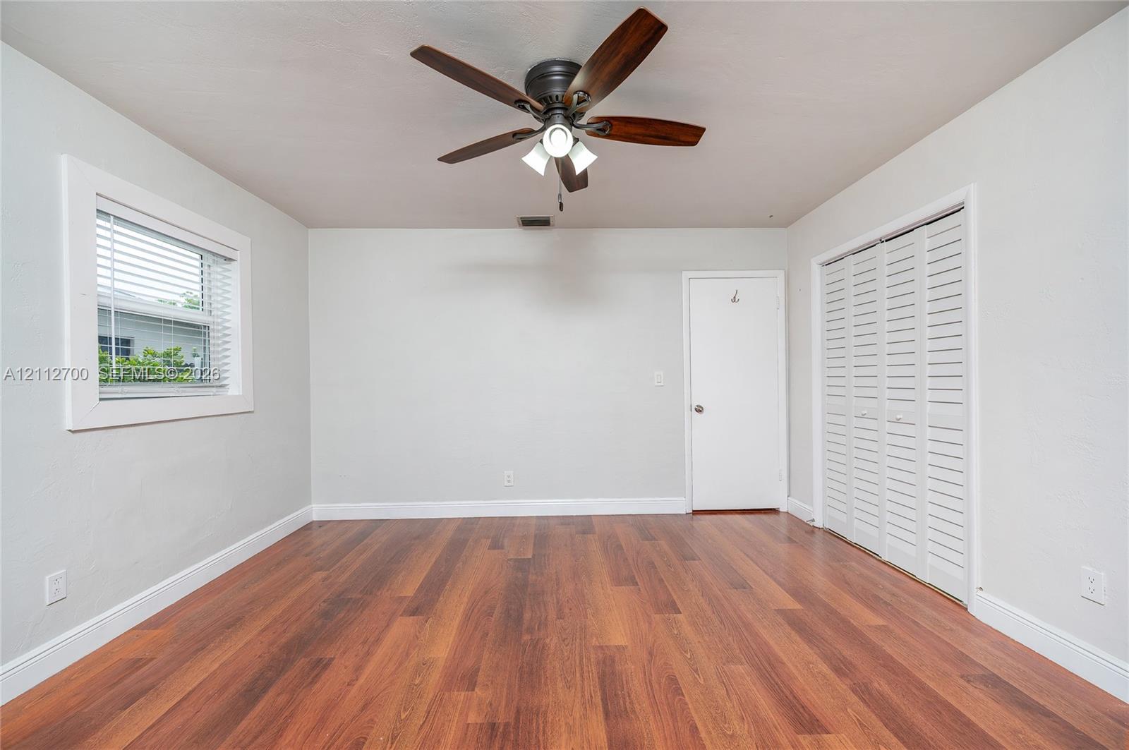 Wood-finish flooring, ceiling fan with integrated lighting, dual-panel closet doors, and window with blinds