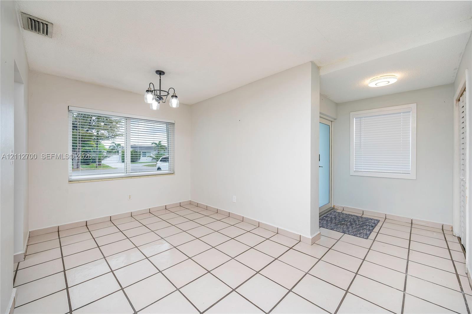 Ceramic tile flooring, multi-light hanging chandelier, and dual windows with integrated horizontal blinds