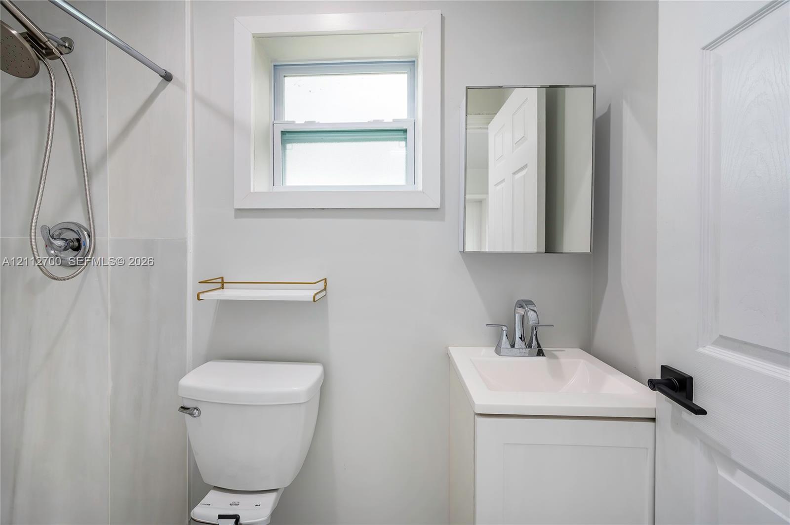 Bathroom featuring a white pedestal vanity, chrome fixtures, a recessed mirror cabinet, and a single-hung window with crisp trim