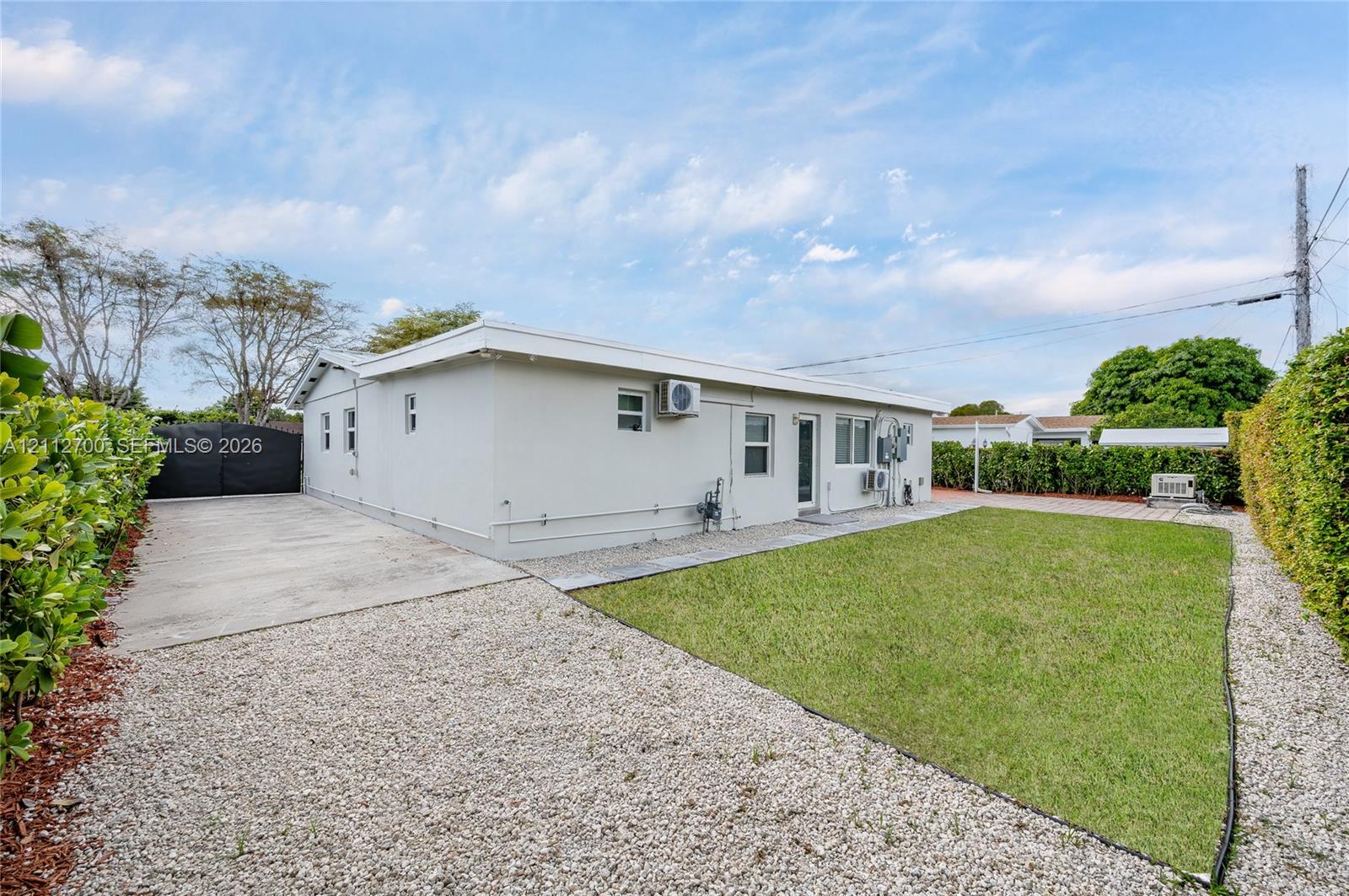 Exterior view featuring a stucco-finish residence with a concrete driveway, gravel hardscaping, and established perimeter hedges