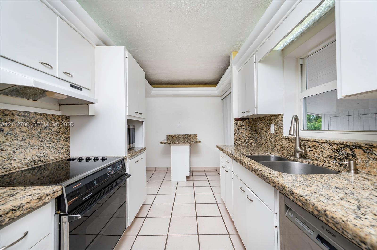 Kitchen featuring stone-finish countertops, tile flooring, white cabinetry, a dual-basin undermount sink, and built-in appliances