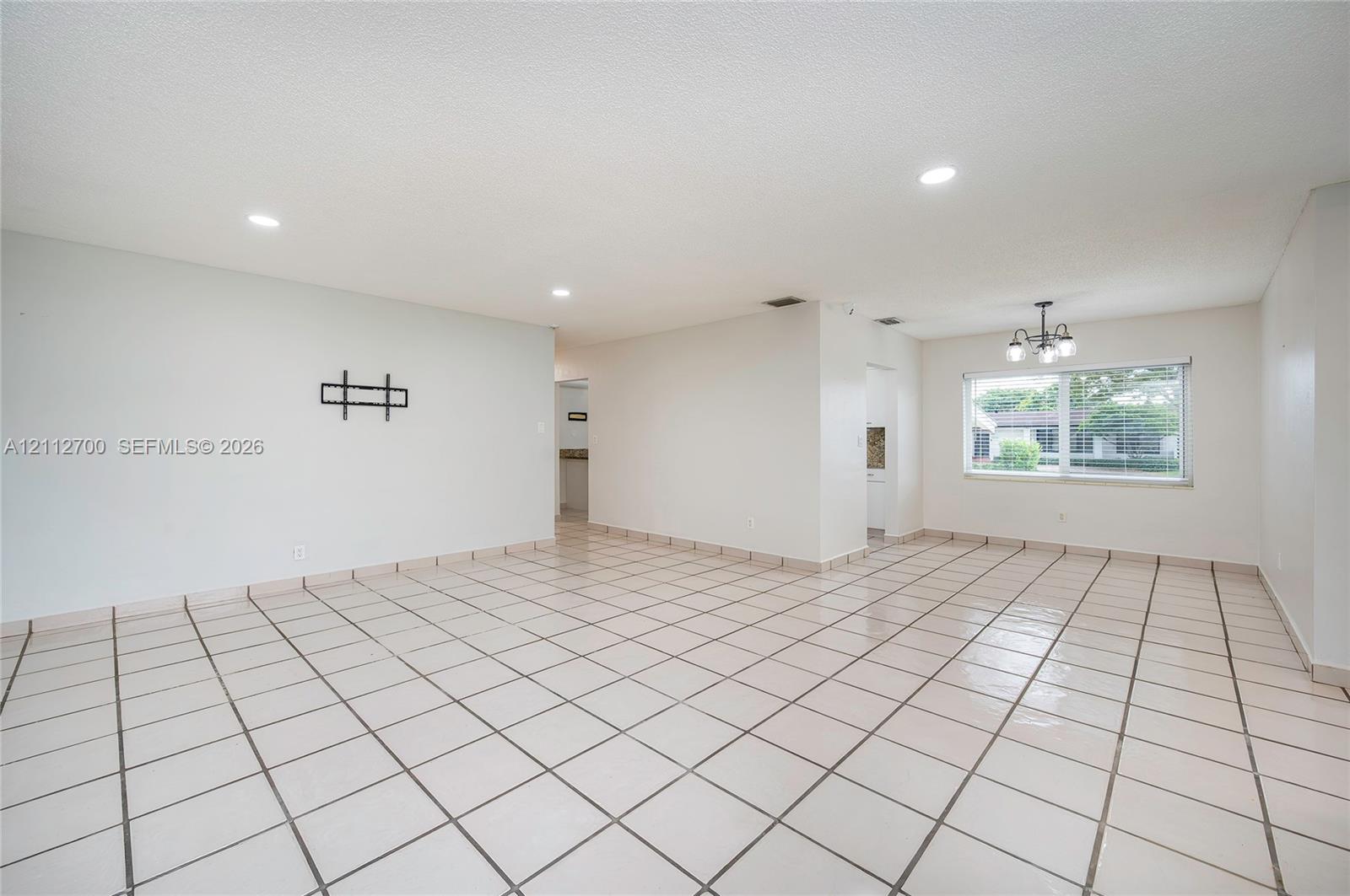 Open-concept room featuring light-toned tile flooring, recessed ceiling lighting, a multi-arm chandelier, and a large window