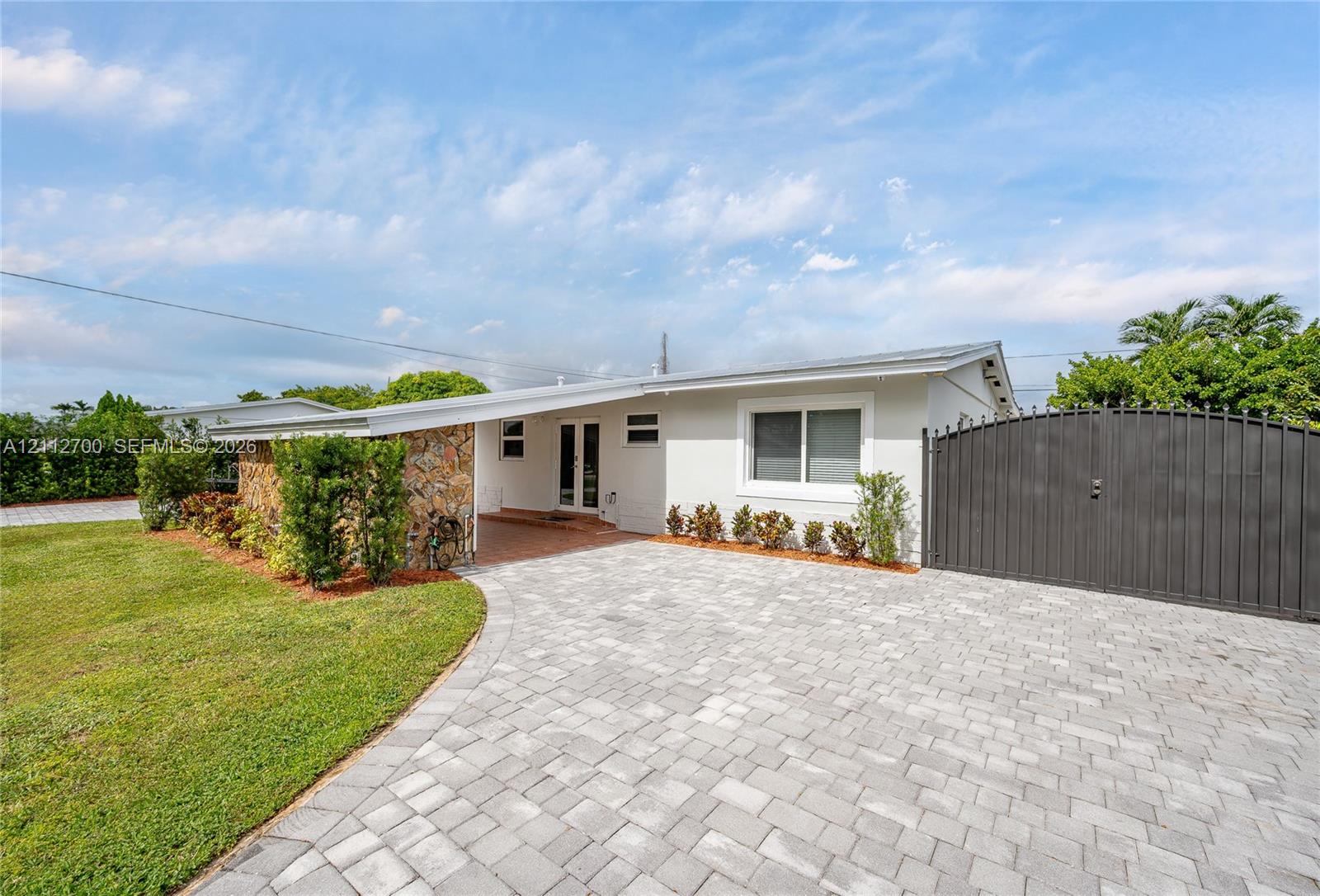 Single-story exterior featuring a stone facade, paver driveway, covered entryway, and privacy gate