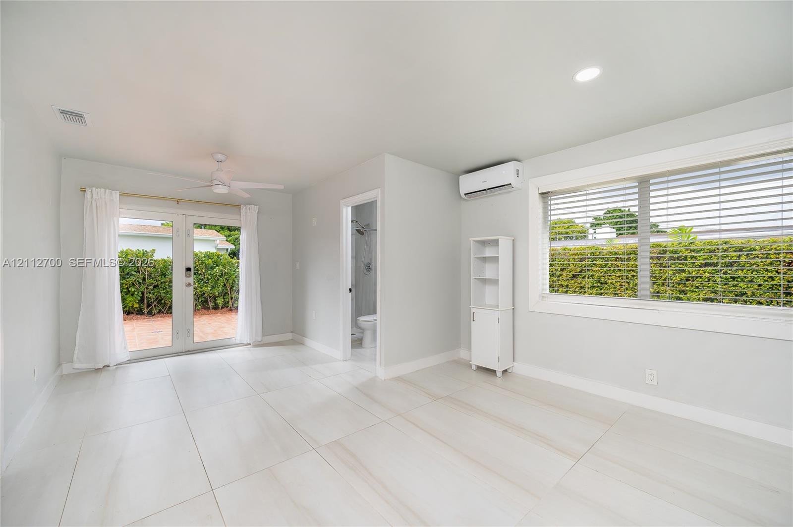 Large-format tile flooring, recessed lighting, ceiling fan, wall-mounted ductless climate control unit, and glass-paned double doors