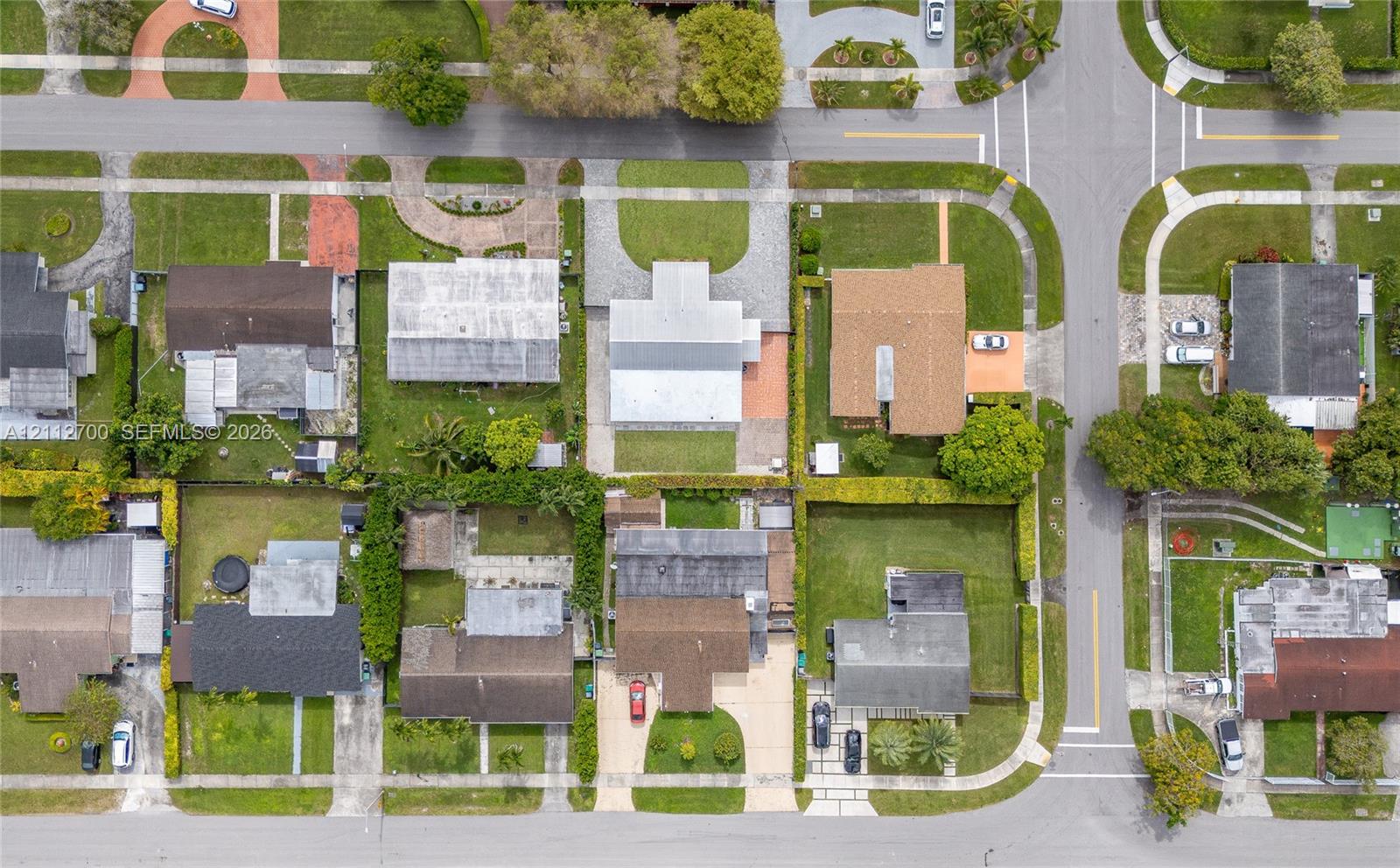 Aerial perspective featuring a corner lot orientation, paved concrete driveways, defined property boundaries, and manicured lawns with mature trees