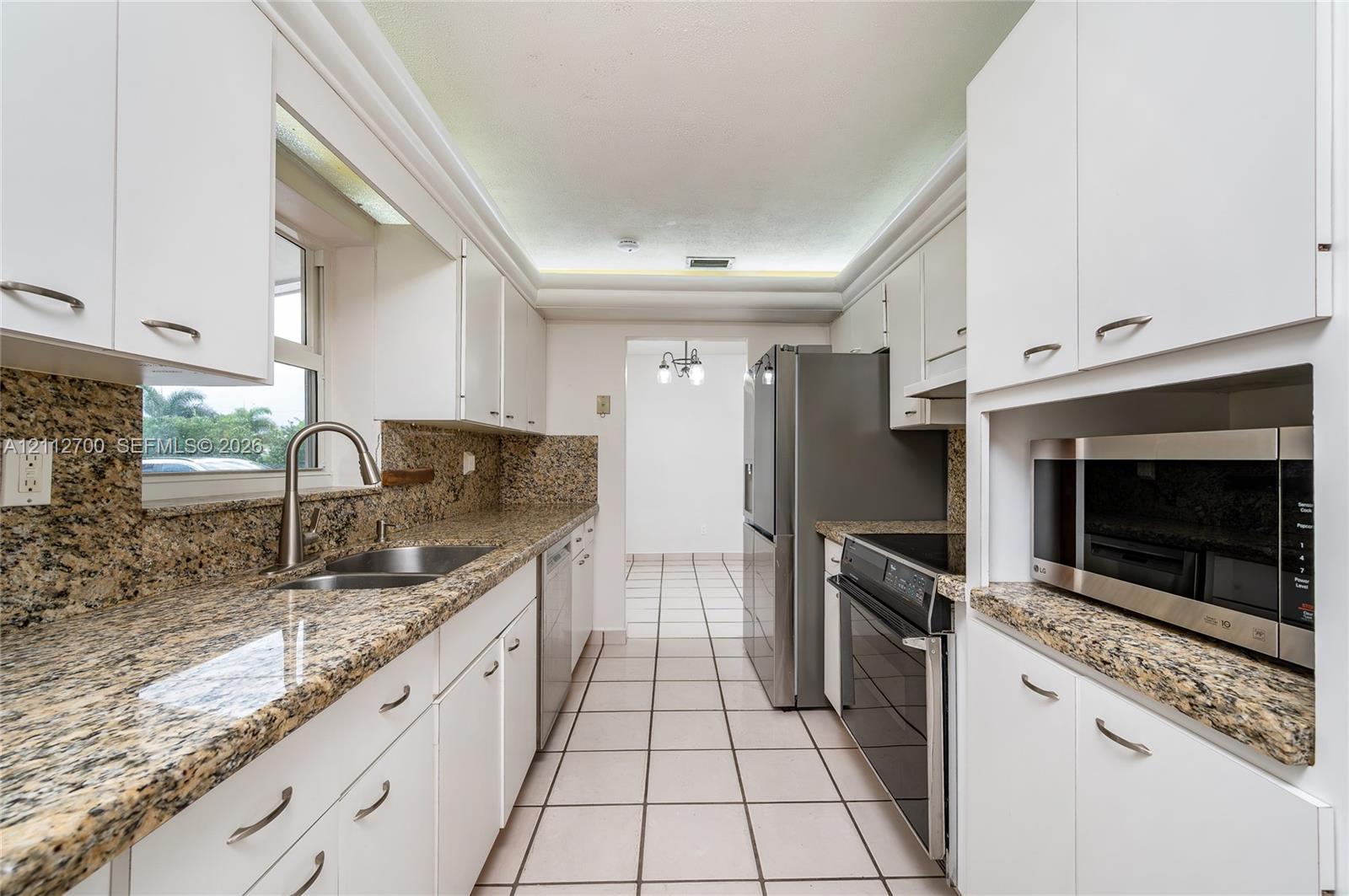 Kitchen featuring stone-finish countertops, white shaker-style cabinetry, stainless steel appliances, tile flooring, and a double-basin stainless steel sink with a high-arch faucet
