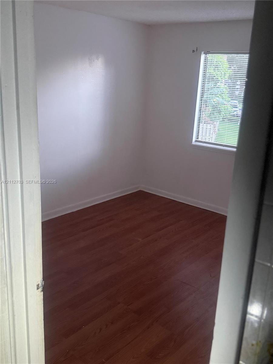 Interior space featuring wood-finish flooring, white walls, and a window with horizontal blinds Interior space featuring wood-finish flooring, white walls, and a window with horizontal blinds