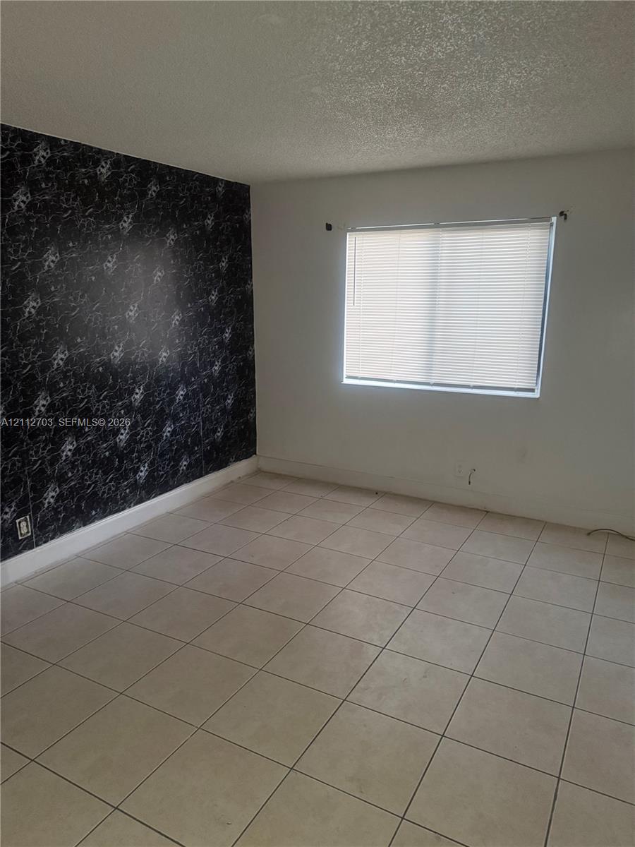 Room featuring large-format ceramic tile flooring, a black-and-white patterned accent wall, and a horizontal window with integrated blinds Room featuring large-format ceramic tile flooring, a black-and-white patterned accent wall, and a horizontal window with integrated blinds