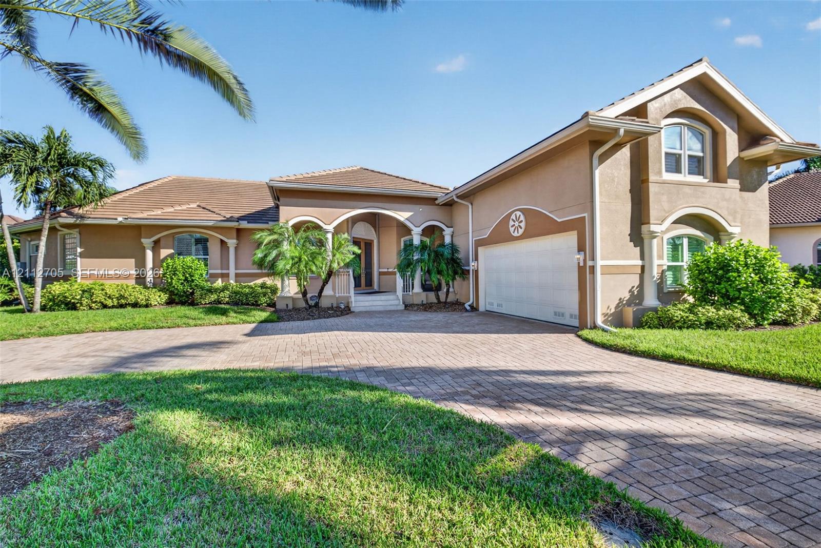 Stucco exterior featuring arched entryways, decorative columns, a tiled roof, and a paved stone driveway