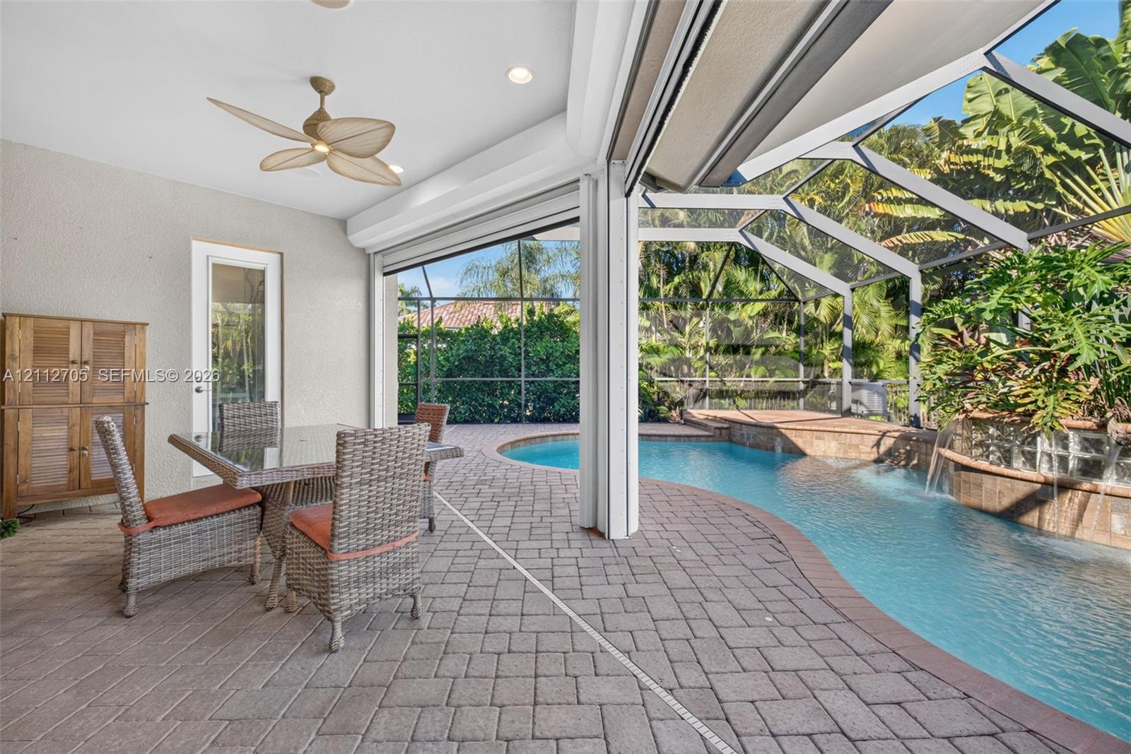 Covered patio featuring paver flooring, a multi-blade ceiling fan, recessed lighting, and a screen-enclosed pool with a water feature