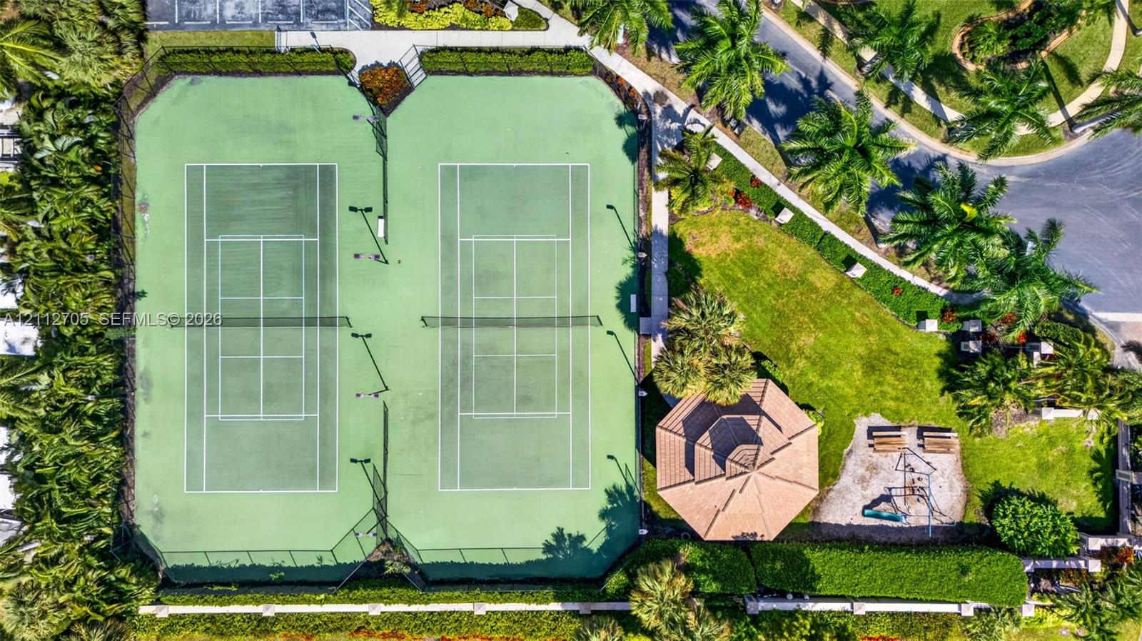 Dual tennis courts featuring perimeter fencing, outdoor lighting, and an adjacent gazebo situated within landscaped grounds