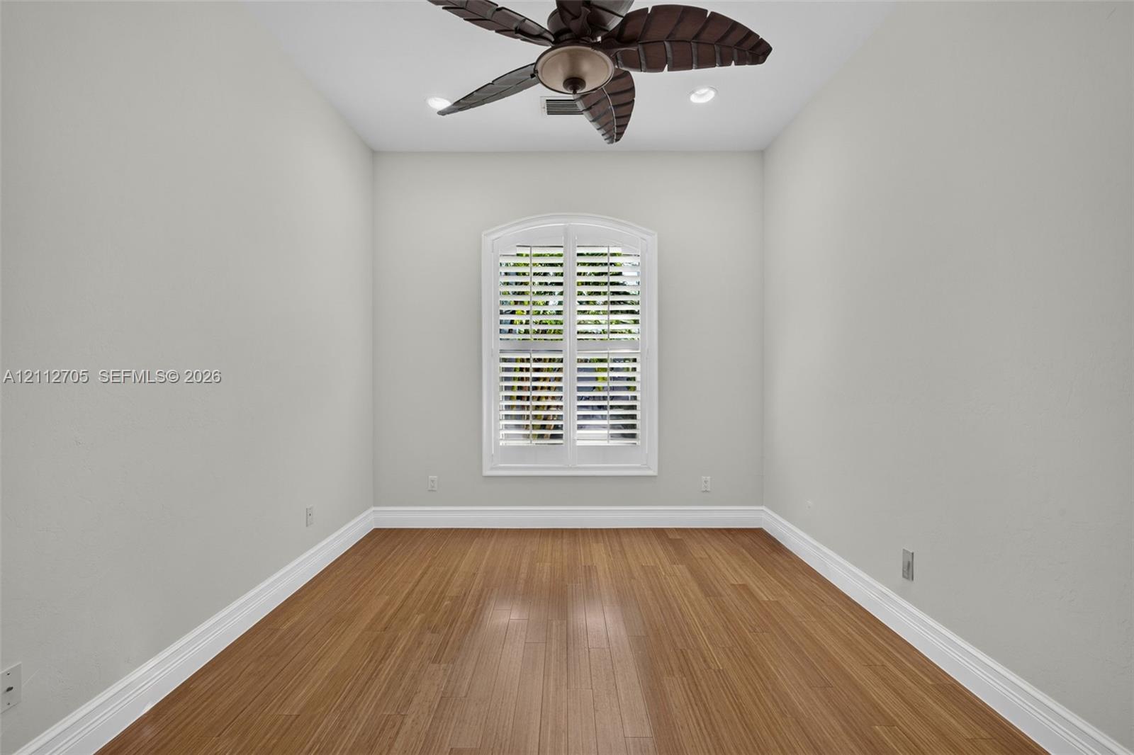 Room featuring wood-finish flooring, recessed lighting, and a multi-blade ceiling fan, accented by an arched window with plantation shutters
