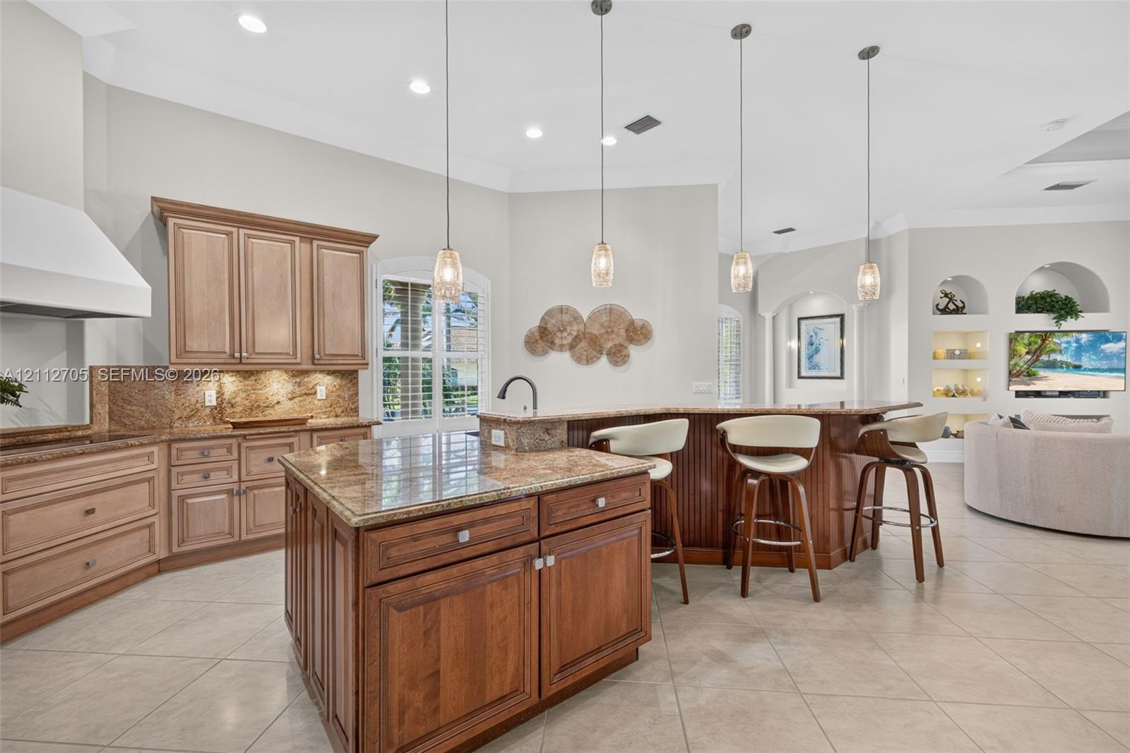 Kitchen featuring custom wood cabinetry, a center island with stone countertops, three suspended pendant lights, and arched built-in wall niches